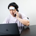 体調不良でベッドに横たわる人がスマホで上司の連絡を見てストレスを感じている様子