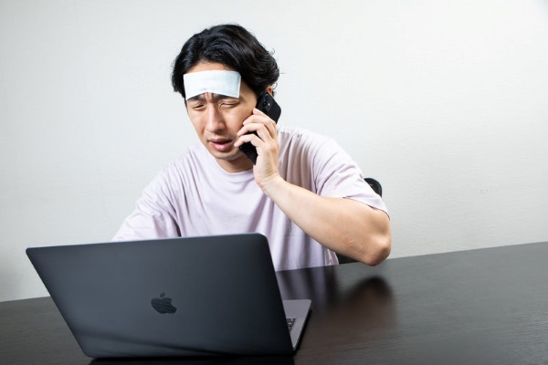 体調不良でベッドに横たわる人がスマホで上司の連絡を見てストレスを感じている様子